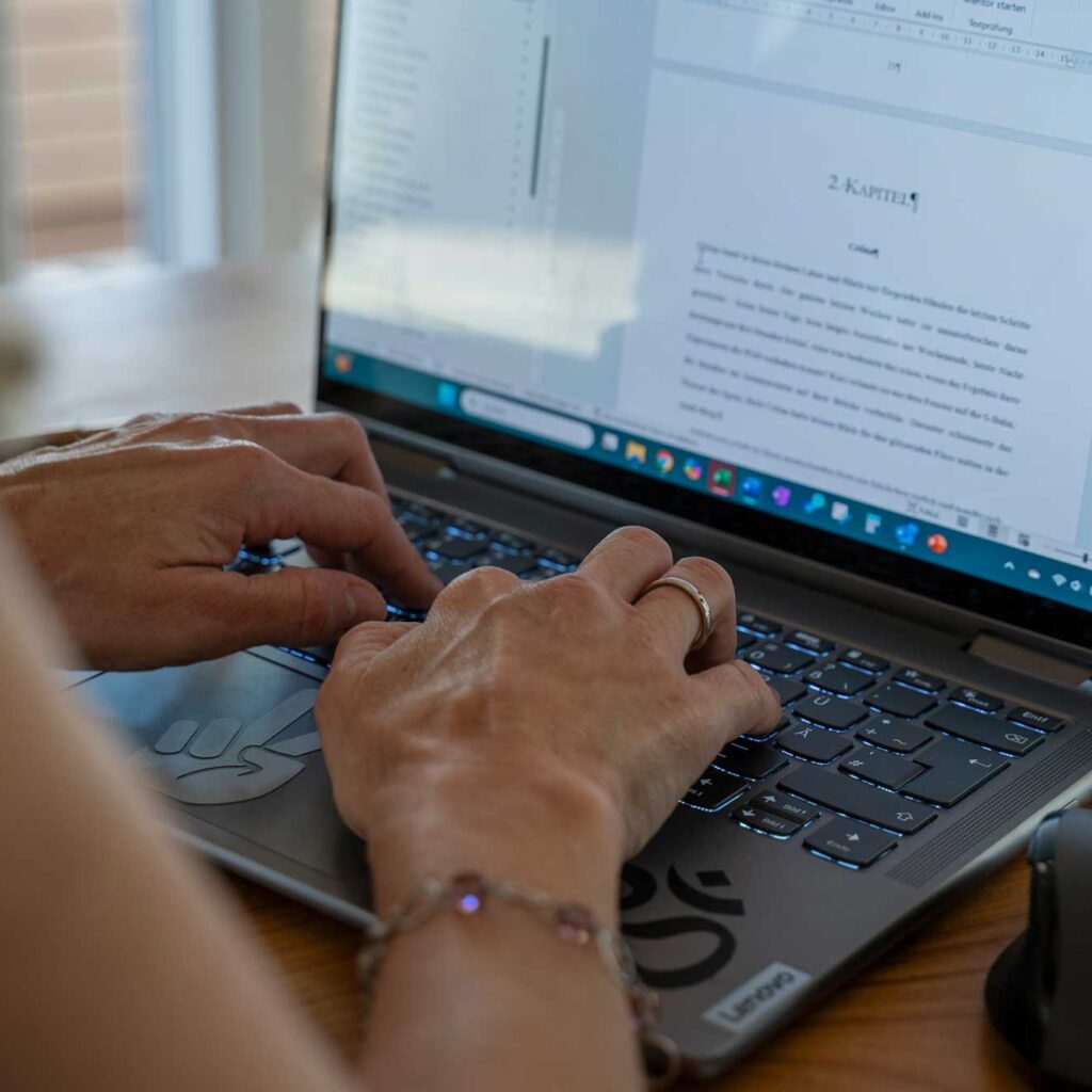 hände tippen auf beleuchteter laptop-tastatur, darüber offenes textdokument sichtbar, rechter bildrand zeigt maus.